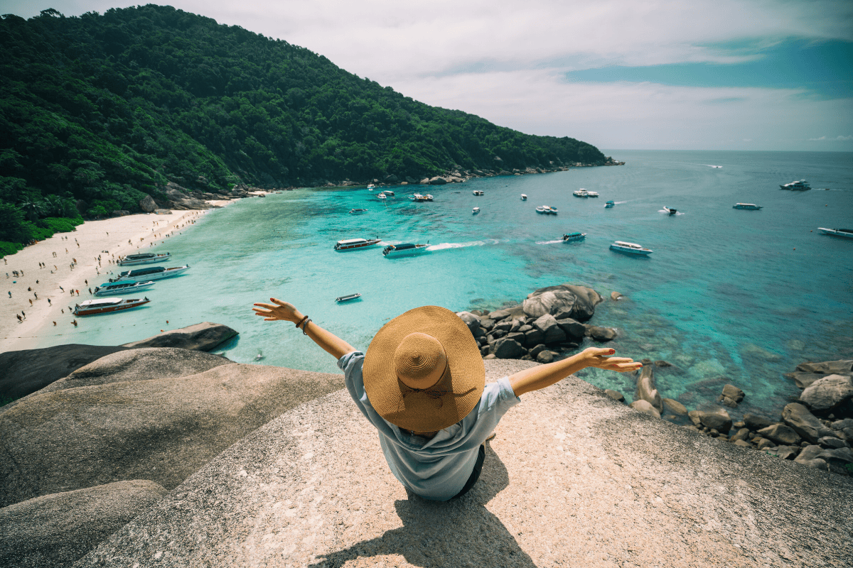 Vue aérienne d'une personne assise sur un point de vue rocheux sur une plage de Phuket.