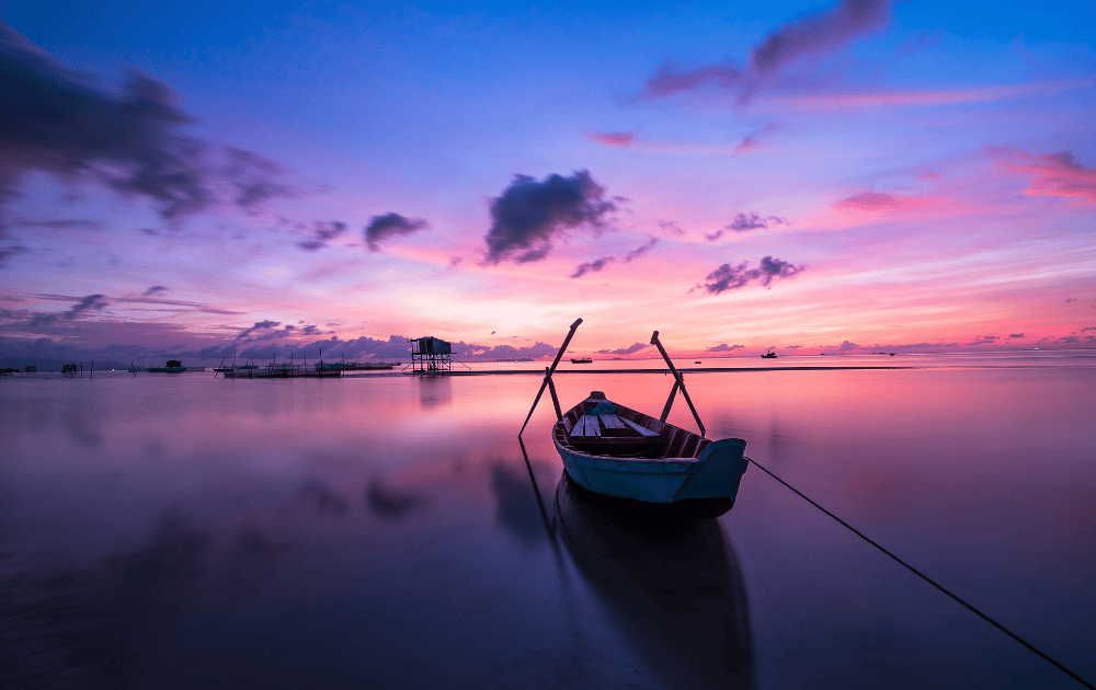 Puesta de sol púrpura y rosa en Tailandia con un pequeño barco al frente