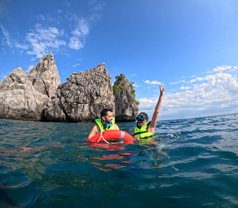 Deux plongeurs avec masque et tuba en gilet de sauvetage flottant près de falaises calcaires dans les eaux claires de Krabi.