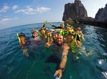 Grupo de buceadores sonriendo y posando para un selfie en el mar con acantilados rocosos al fondo