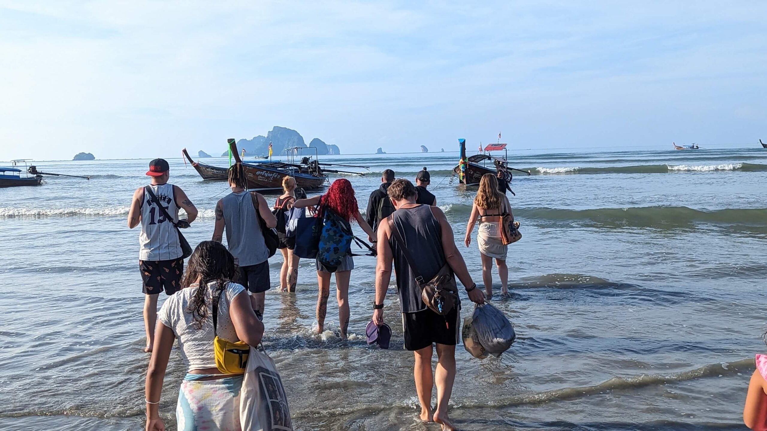 grupo de personas vadeando el agua hacia una barca de cola larga en krabi
