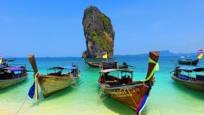 longtail boats on phranang beach in railay with island rock in the background