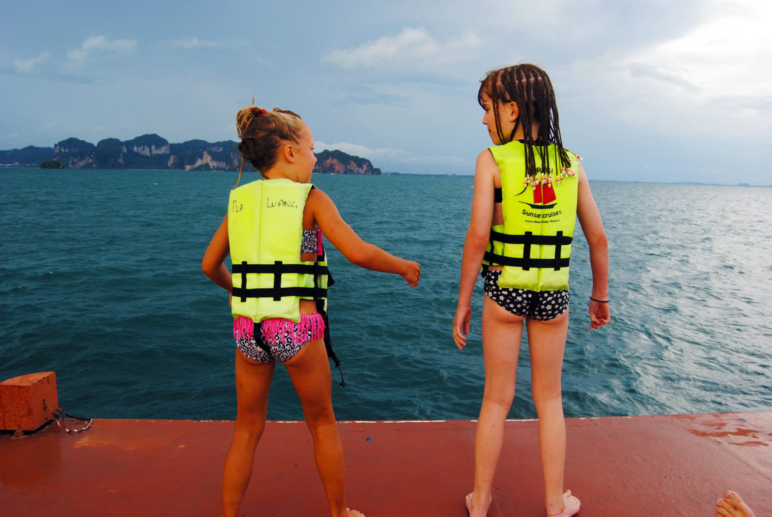 2 chicas jóvenes listas para saltar de la cubierta de un barco con krabi en la distancia