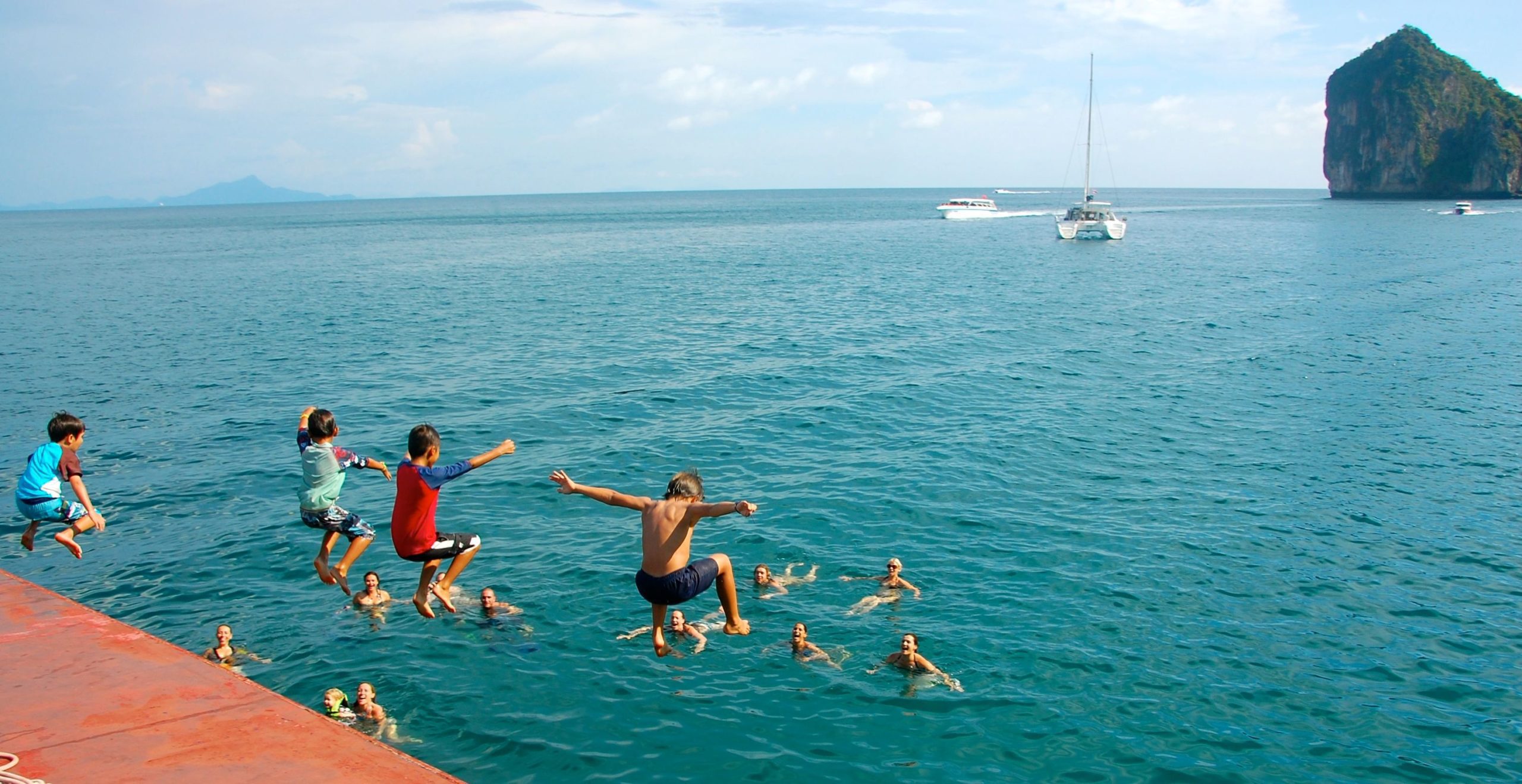 Niños saltando desde la cubierta de un crucero matinal en Krabi con sus padres en el agua