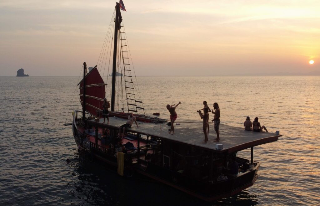un homme sur le point de sauter du bateau pirate krabi sunset cruise sur le pont supérieur pendant que les gens regardent et que d'autres regardent le lever du soleil en arrière-plan
