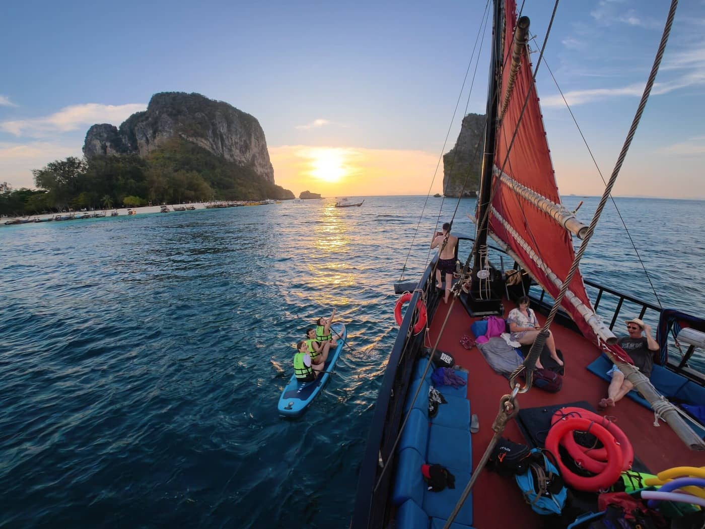 Des visiteurs pratiquant le paddleboard à côté du bateau traditionnel en bois de Krabi Sunset Cruises au coucher du soleil, près de Railay, à Krabi