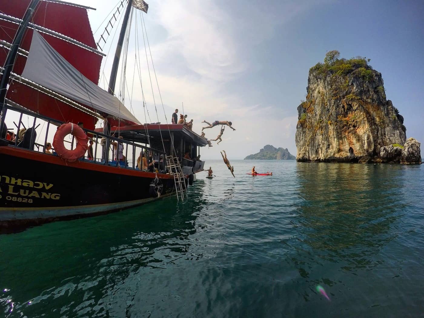 Guests jumping from the roof of a junk boat into the sea beside a limestone island in Krabi.