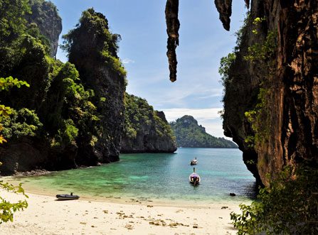 Imagen de embarcaciones en la playa de Railay, en Krabi (Tailandia), con aguas transparentes, arena blanca y rodeada de acantilados rocosos.