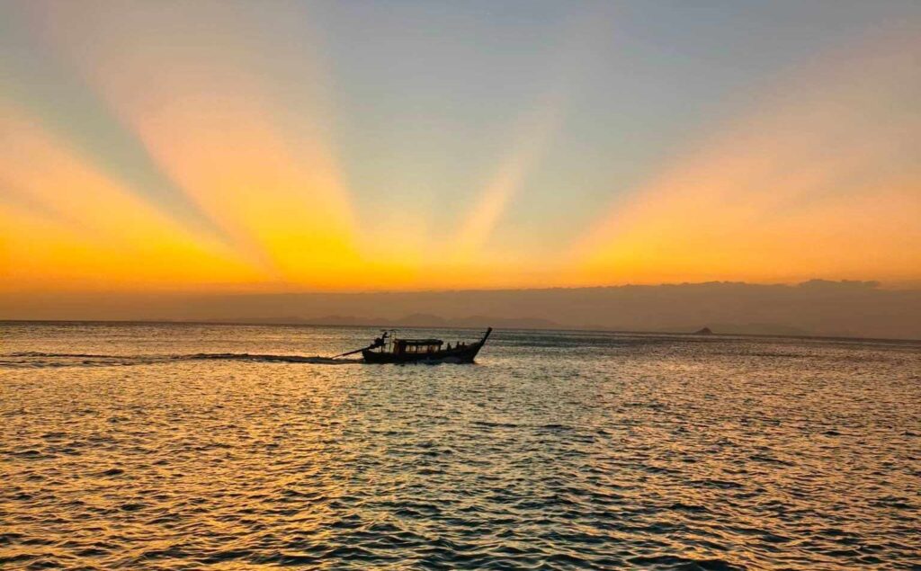 un barco de cola larga en el agua cerca de la playa de aonang durante la puesta de sol
