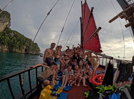 Grupo de invitados felices posando y celebrando en un barco junco de vela roja en Krabi