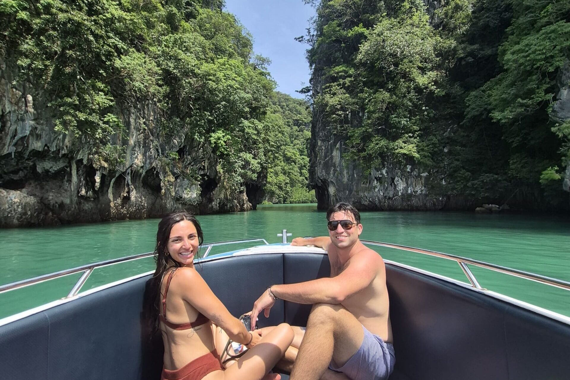 A couple sitting at the front of a speed boat in Krabi with limestone cliffs behind them.