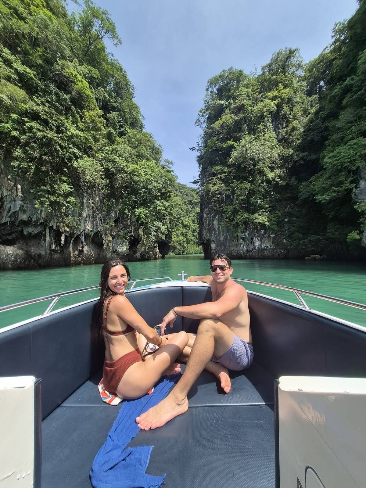 Una pareja sentada en la proa de una lancha motora en Krabi, con acantilados de piedra caliza a sus espaldas.
