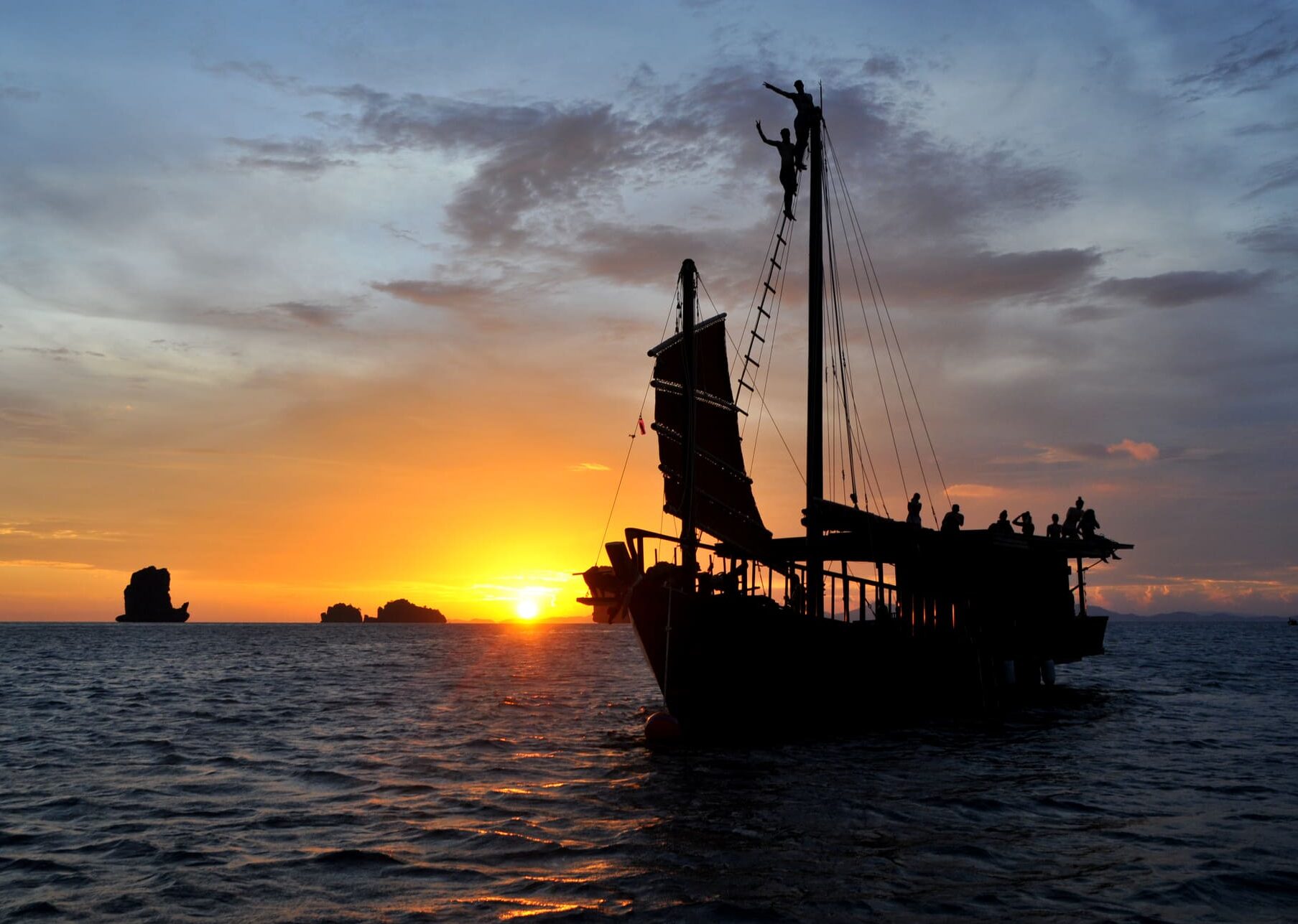 Junk boat at sunset in Krabi with 2 people climbing the mast