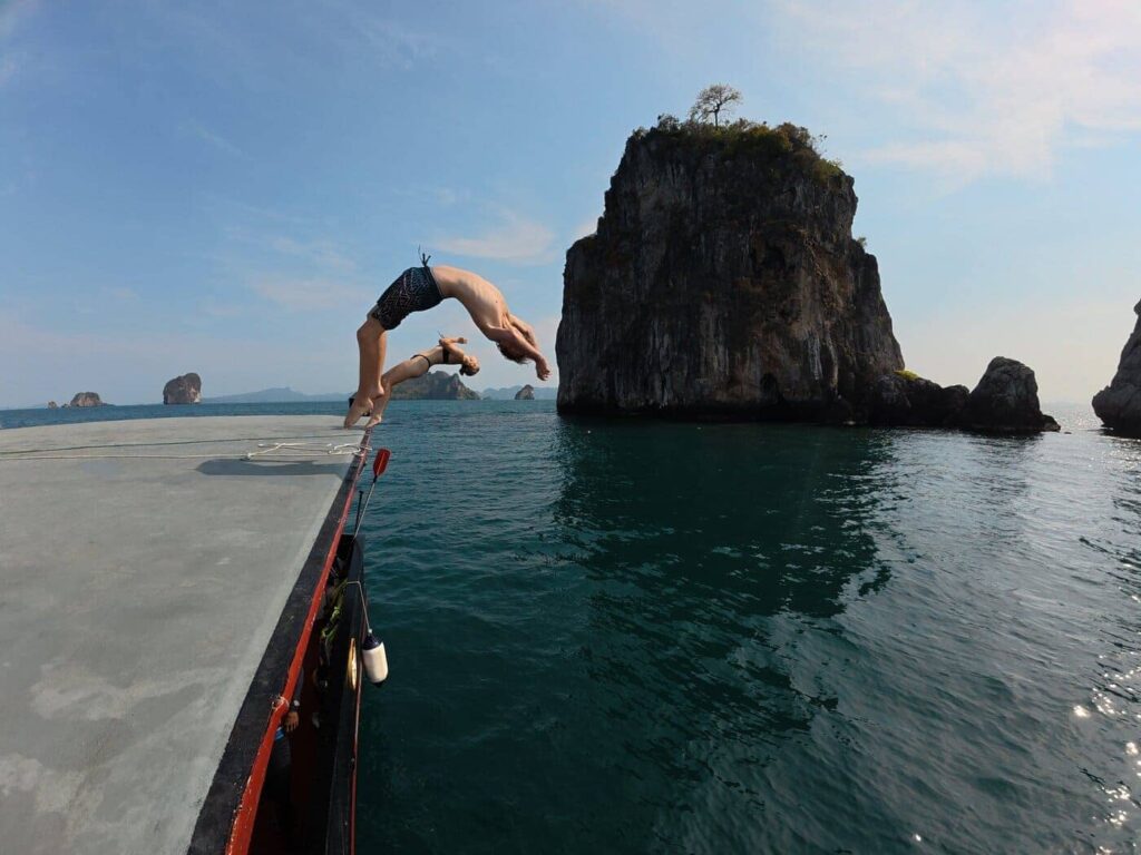 Two guests flipping from the rooftop deck of Pla Luang into the sea beside a limestone island in Krabi.