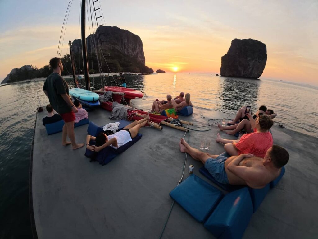 Guests relaxing on the rooftop deck of a junk boat while watching the sunset between limestone islands in Krabi